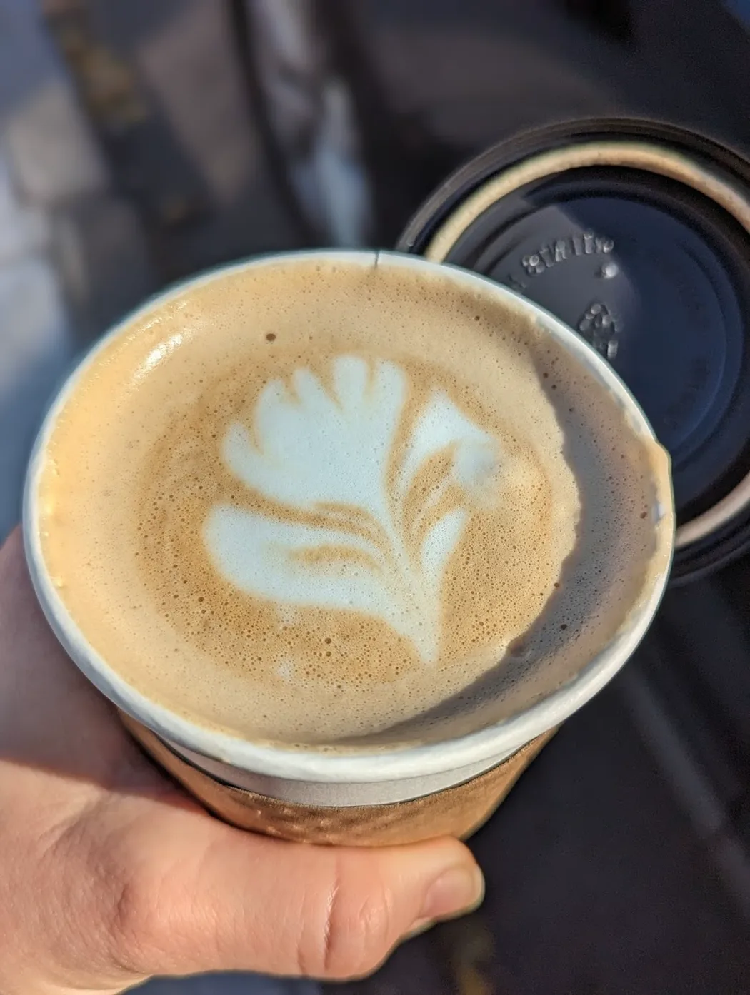 An oat-milk latte with tulip latte art, held in hand